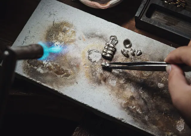 Close-up of a jeweler using a blowtorch to craft silver jewelry pieces on a workbench.