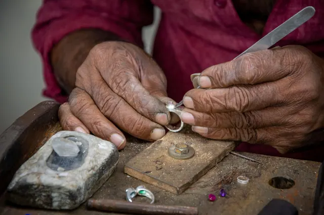 Close-up of a skilled artisan crafting a silver ring by hand at a workshop desk.
