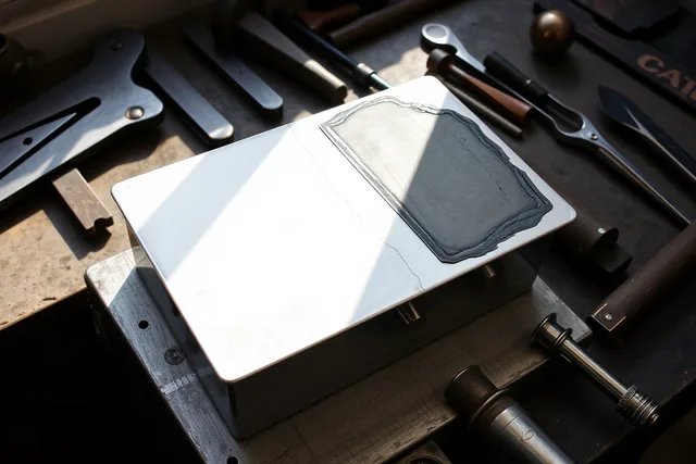 Silversmith's bench with a partly formed silver box, files, hammer and visible scratch. Silversmithing workmanship problems: poor fit, distorted metal and heat damage