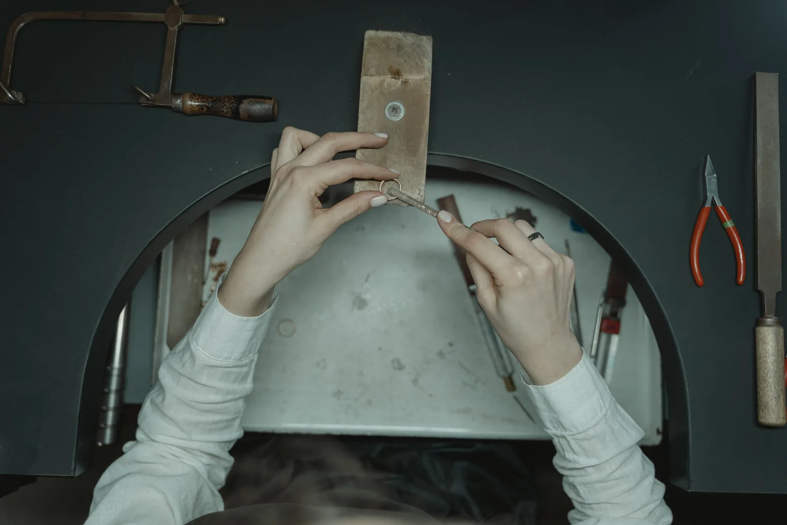Top-down view of a jeweler's hands crafting with tools on a workbench. Saw frame, blade and bench pin checklist before cutting