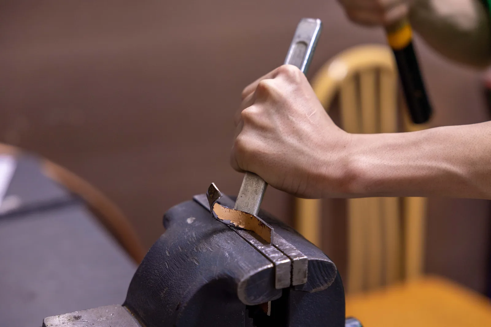 Detail of a hand using a hammer and chisel on metal in a workshop setting. Silversmithing Studio Safety: Hazards and Controls