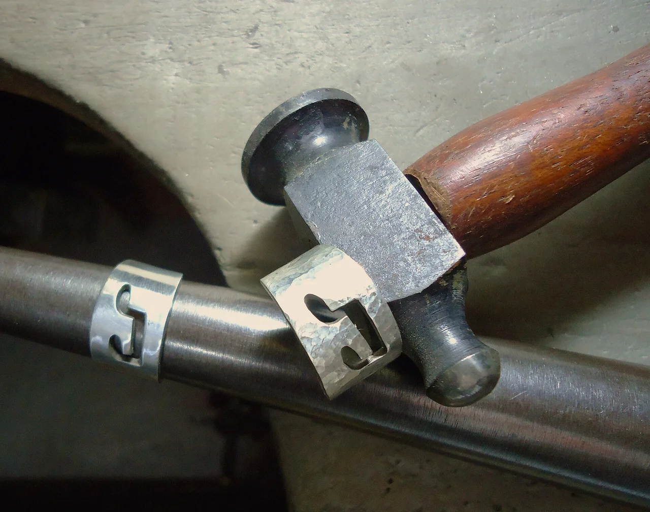Two silver rings on a mandrel beside a hammer during forming and finishing work