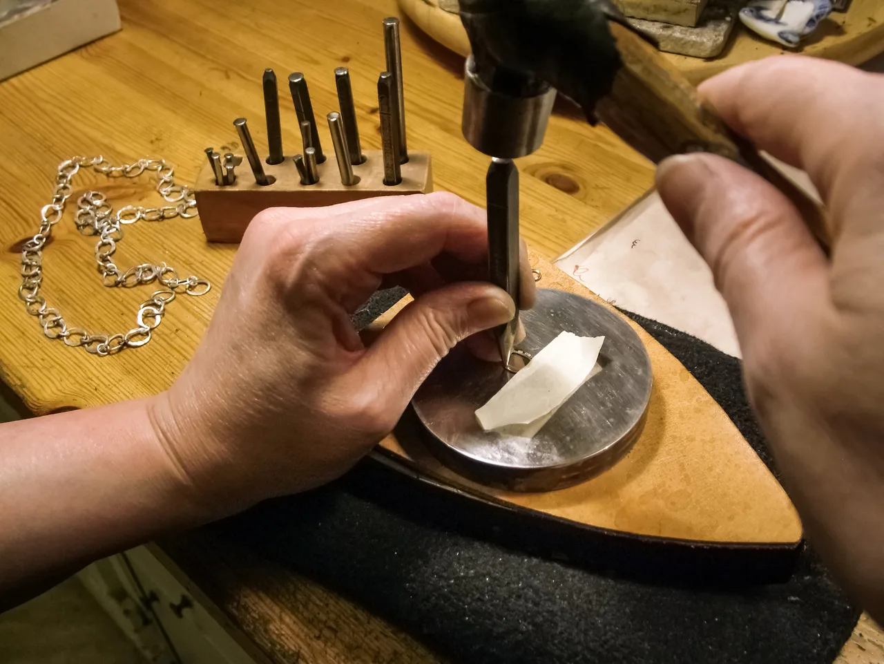 A silversmith holding a punch upright while striking a mark into a supported silver ring